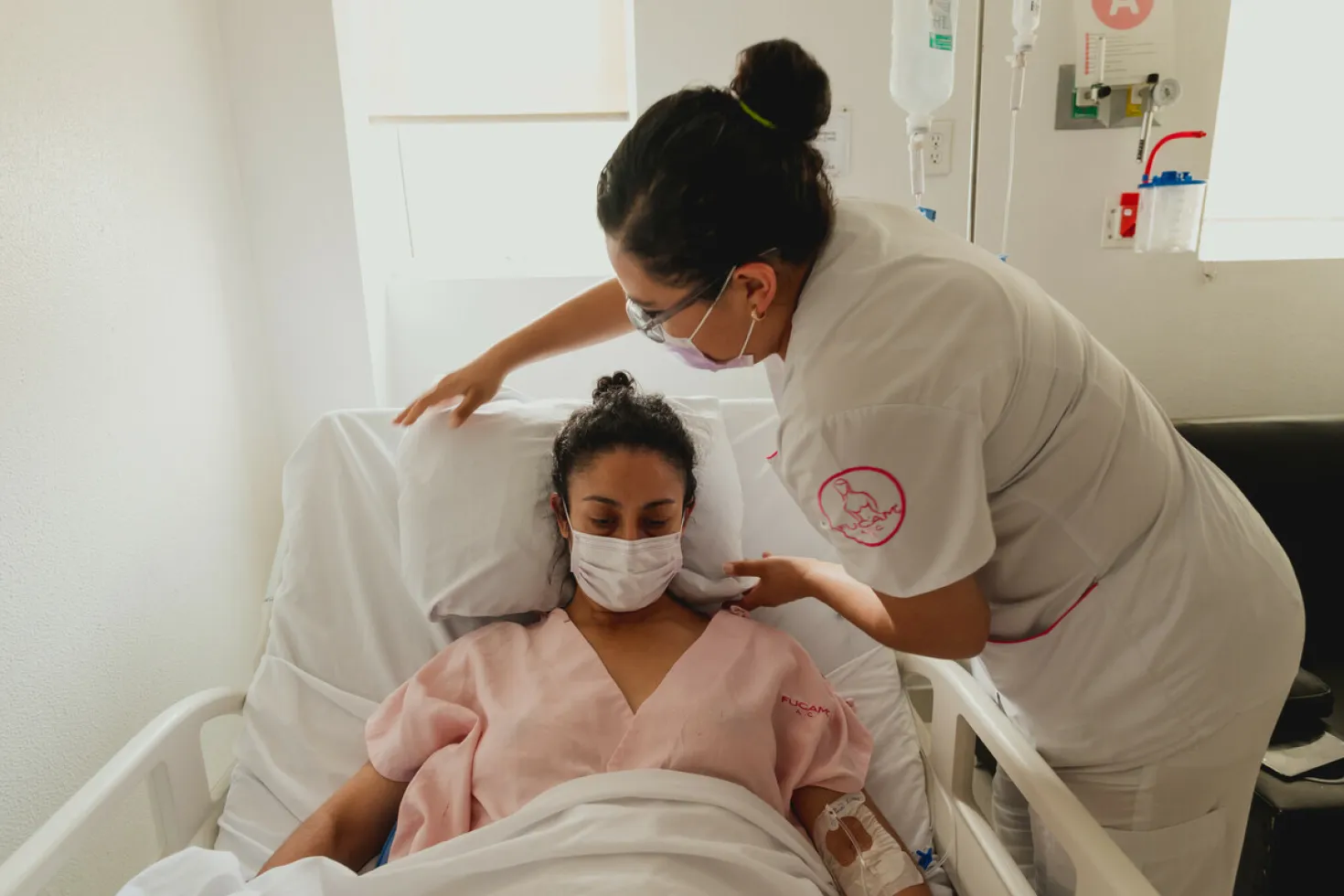 A nurse helps a patient at the hospital - both are wearing a mask