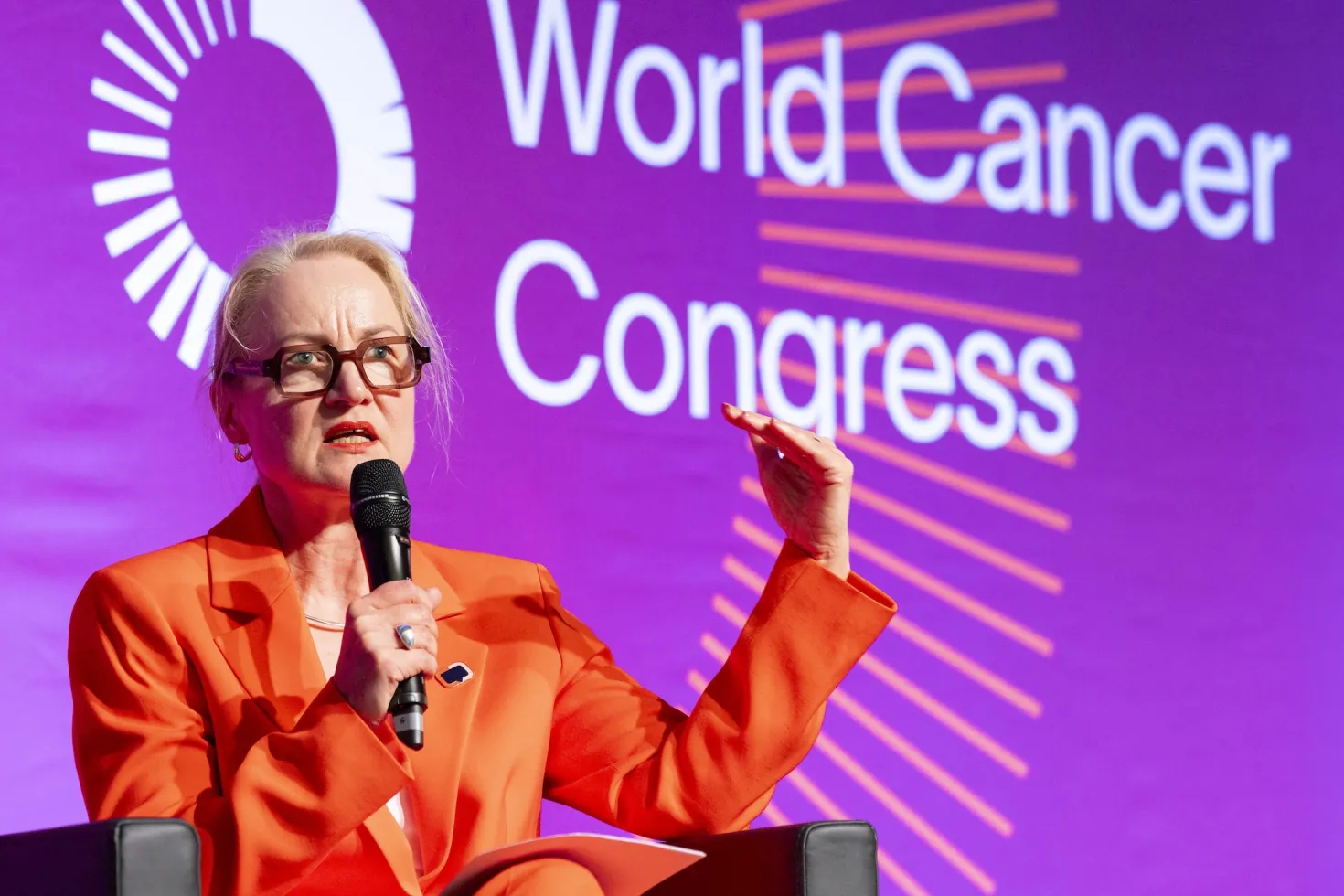 UICC President Ulrika Årehed Kågström wearing an orange suit speaking at the World Cancer Congress