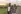 A senior woman with cancer walks with her adult daughter at sunset down a rural road. The affectionate pair are talking and walking with arms linked.