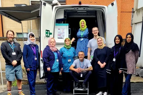 A Caucasian man with women wearing headscarves working for the World Hepatitis Alliance posing before a service van
