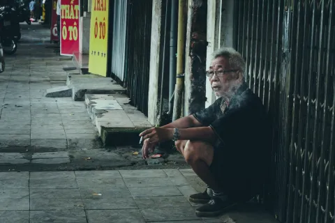 Tobacco kills more than 8 million people each year, according to WHO. The tobacco industry is engaged in a number of actions to undermine national health policies and efforts by governments to curb smoking in their countries. Older man kneeling near a shop, smoking a cigarette