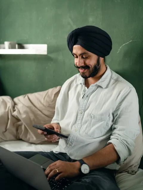 Man with turban consulting his laptop and mobile phone